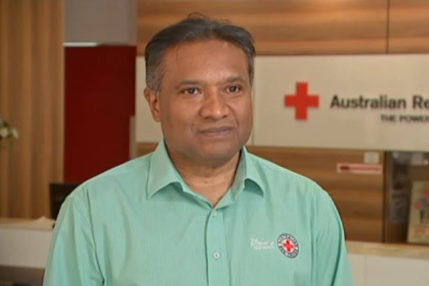 A man in a green shirt sits in front of an Australian Red Cross sign.