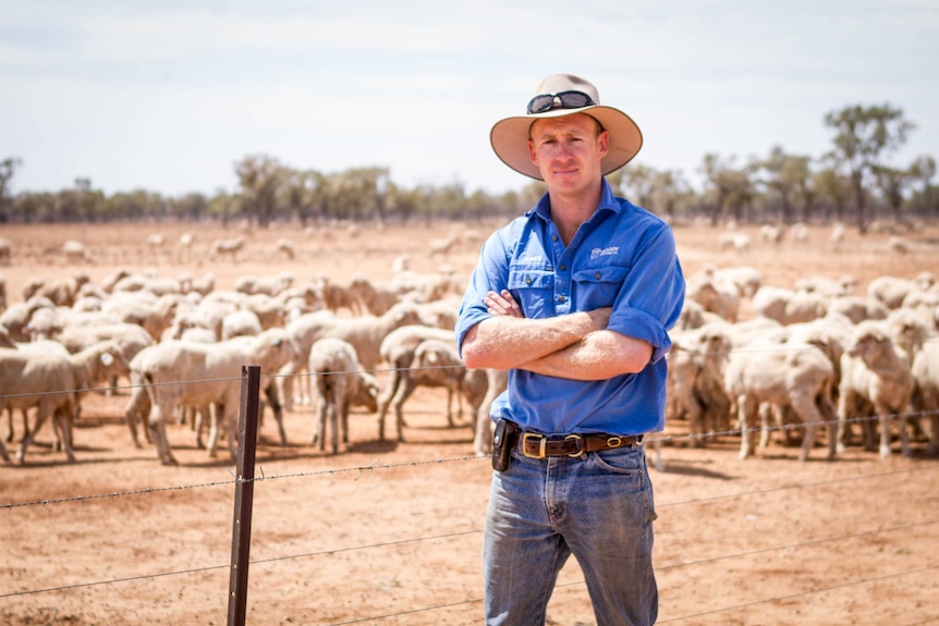 Young grazier Jesse Moody stands in next to paddock full of sheep.