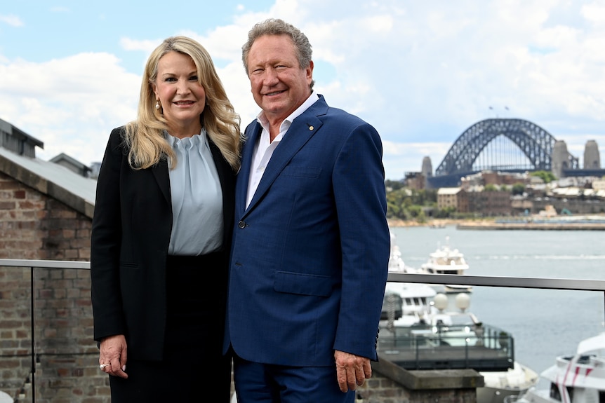 A woman with long blonde hair, Elizabeth Gaines, stands smiling with Andrew Forrest on Sydney Harbour.