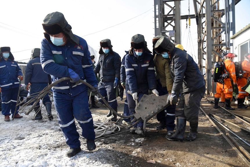 Rescuers in blue suits work at the site of the gold mine