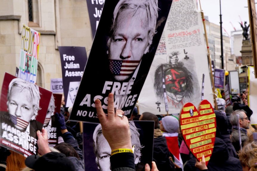 A large crowd of people holding signs with supportive slogans of Julian Assange