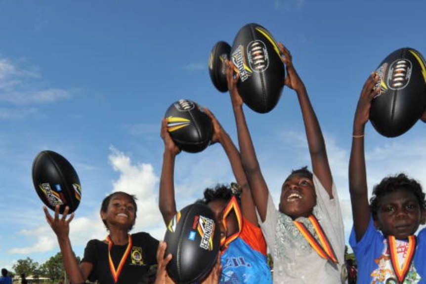 Indigenous children cheering and holding AFL balls