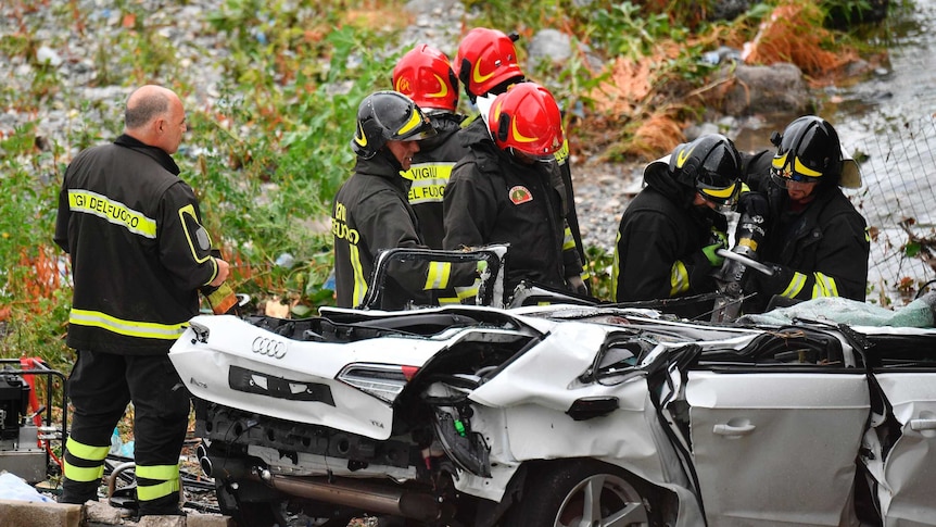 Rescuers work to recover an injured person from a crushed car.