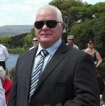 Gerard Dezoete wears a suit and tie and dark sunglasses and looks at the camera with a serious expression