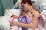 Mother Jessica Linwood attached to medical equipment asleep with her daughter Harper on her chest.