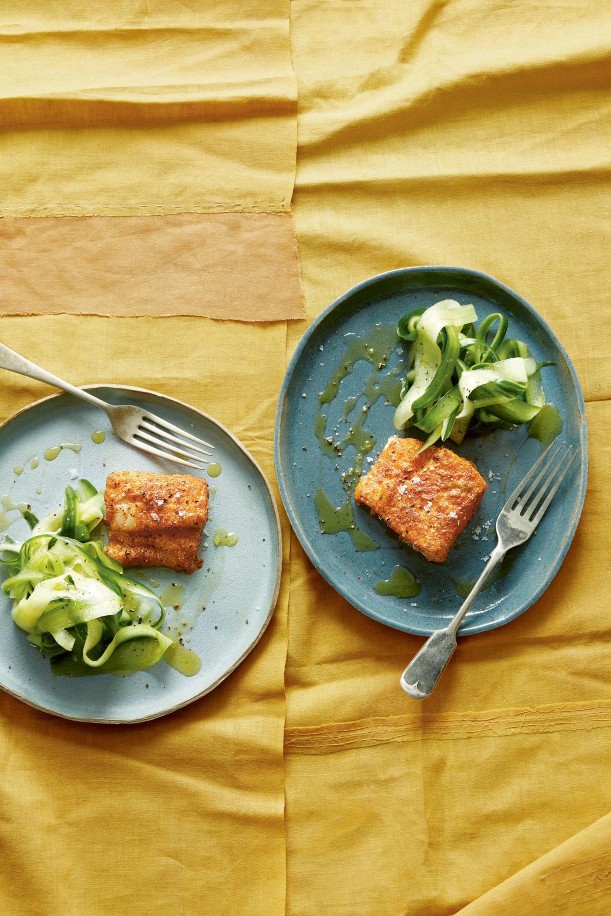 Two plates with pieces of fried cod alongside a salad of crunchy cucumber are placed on a table
