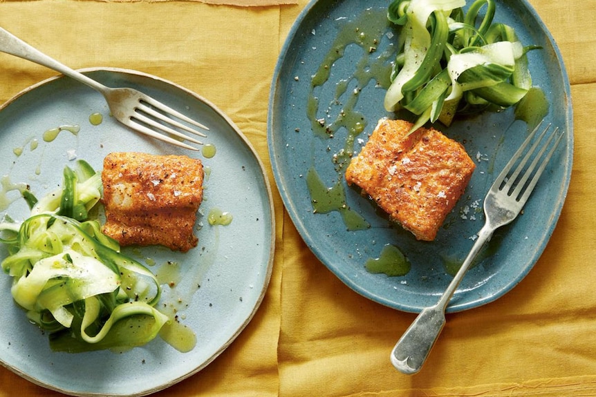Two plates with pieces of fried cod alongside a salad of crunchy cucumber are placed on a table