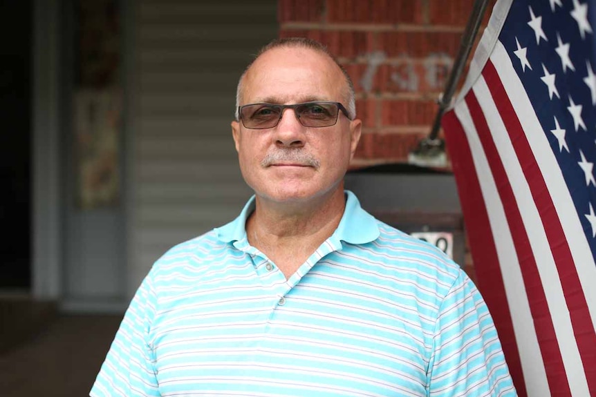 Bobby Borders stands in front of an American flag and looks at the camera.