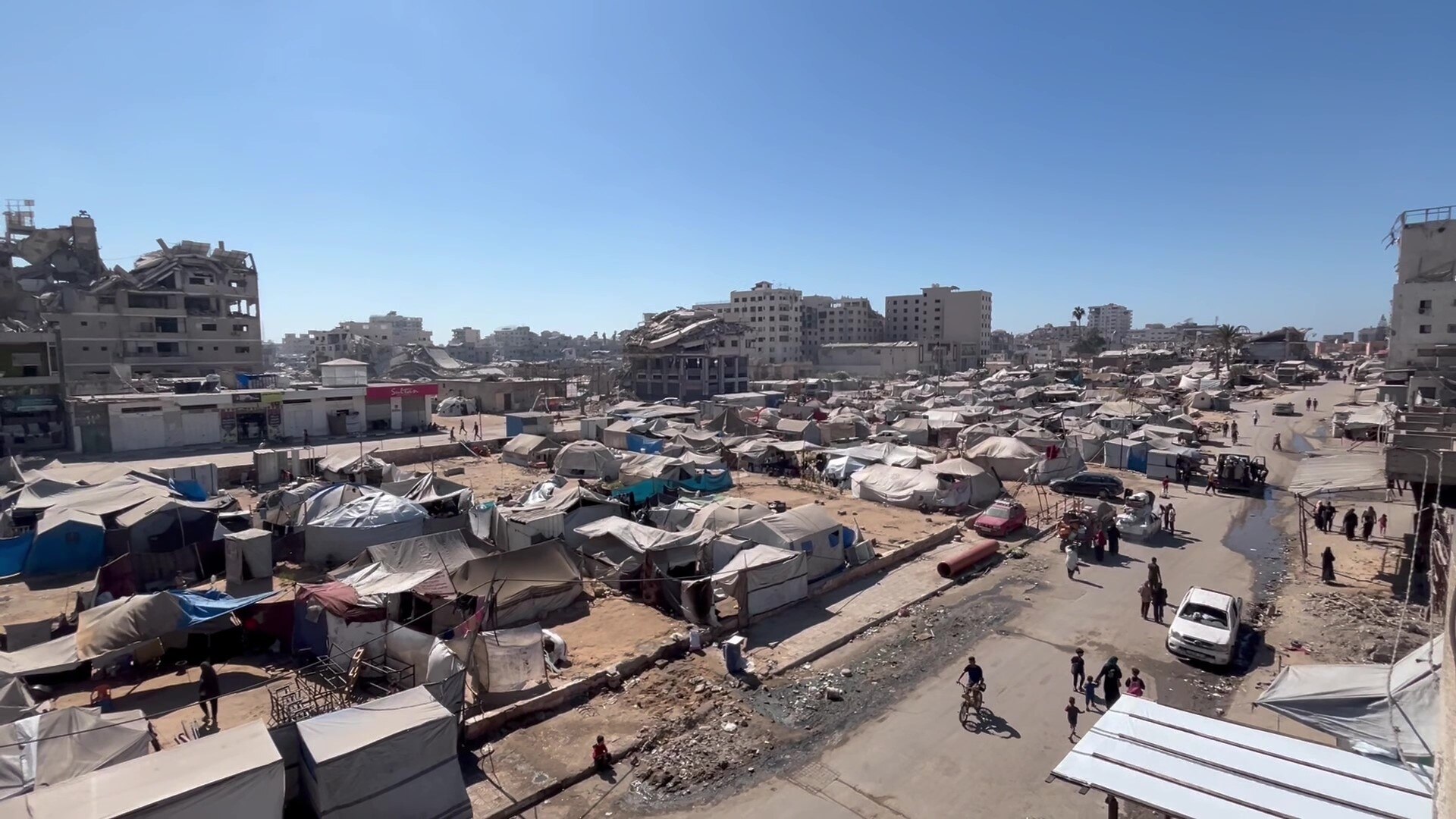 Dozens of tents pitched on dirt in front of collapsed buildings.