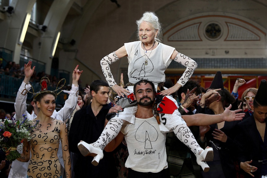 Vivienne Westwood sits on top of a man's shoulders in outlandish fashion/ 