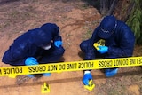 Two police officers in blue coveralls put markers near crime scene.