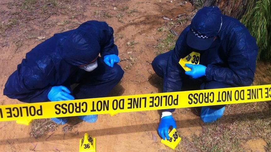 Two police officers in blue coveralls put markers near crime scene.