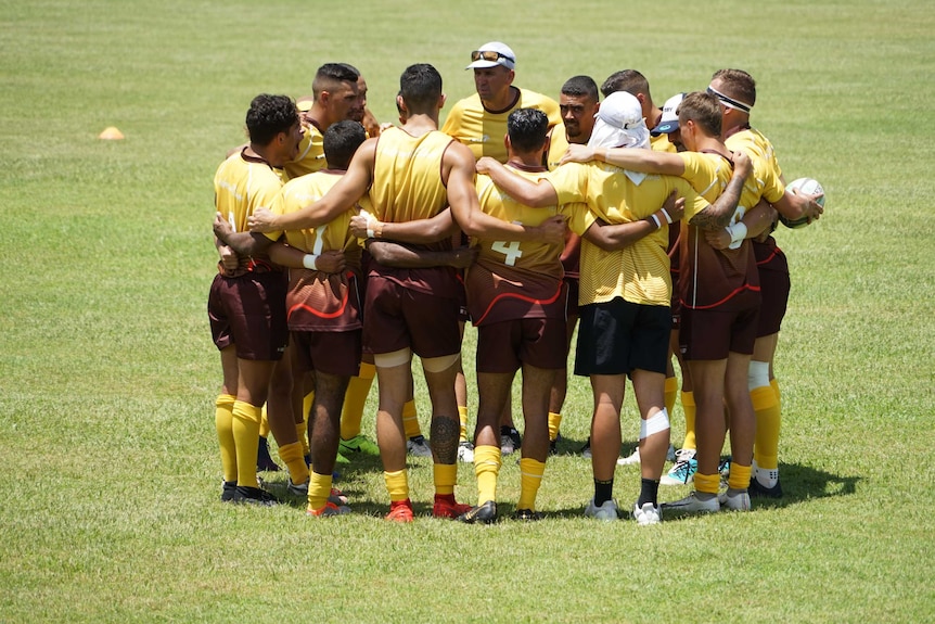 A team of First Nations rugby players huddle and listen to their coach.