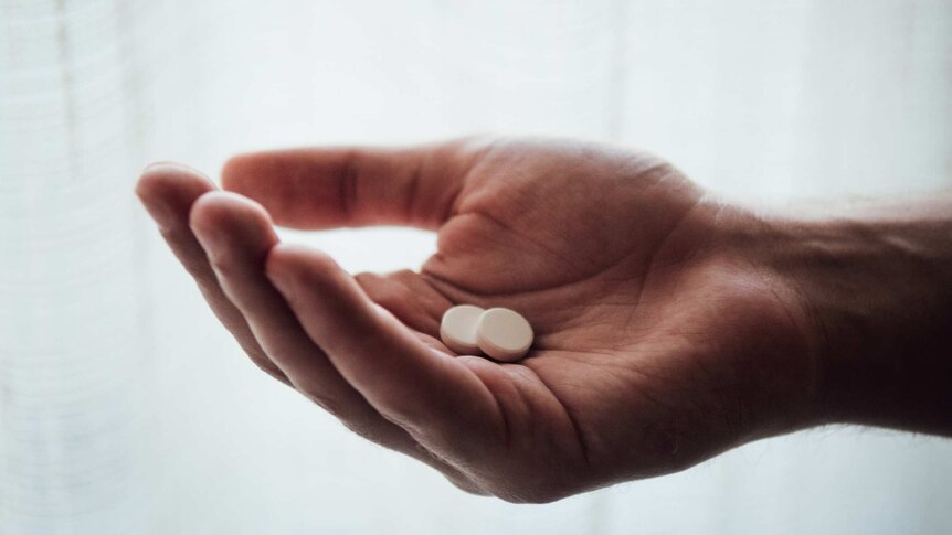 close up of hand holding two pills against white curtain background