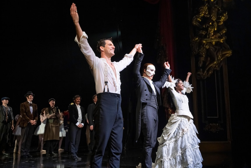 Three people in costume with their arms raised to take a bow on stage