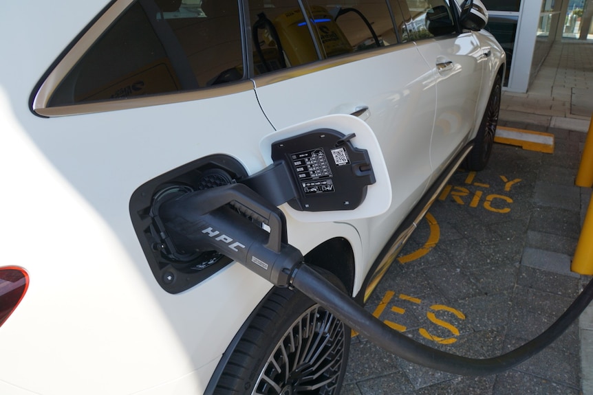 A car parked at an electric vehicle charging station, with the charger attached.