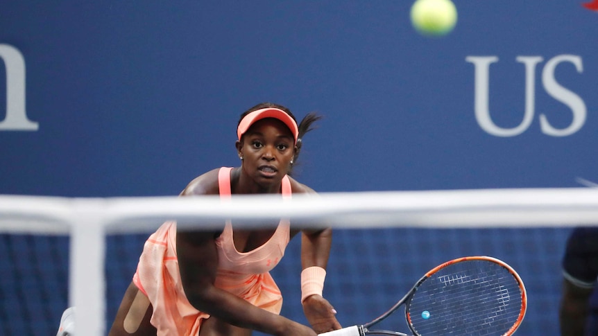 Sloane Stephens follows through after a serve. The ball is seen above the net in the foreground.