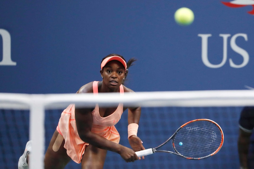 Sloane Stephens follows through after a serve. The ball is seen above the net in the foreground.