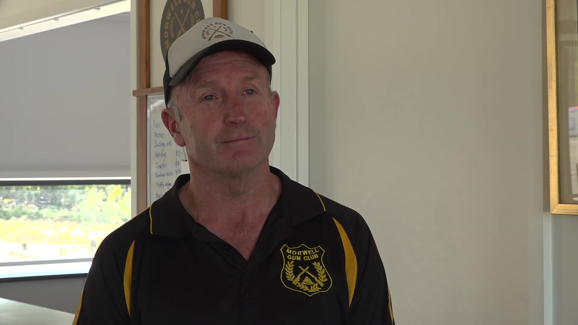 Homem usando um boné branco e uma camisa polo preta e dourada dentro de uma sala de clube.