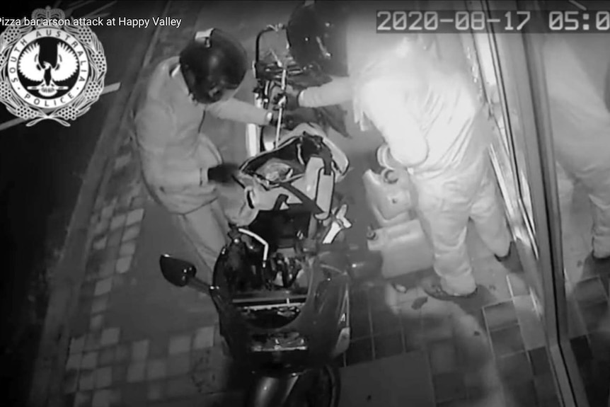 CCTV footage of two people wearing motorbike helmets standing over a motorbike.