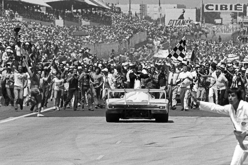 The winning car of the Le Mans 24 Hours arrives at the chequered flag, with thousands of people on the race track.