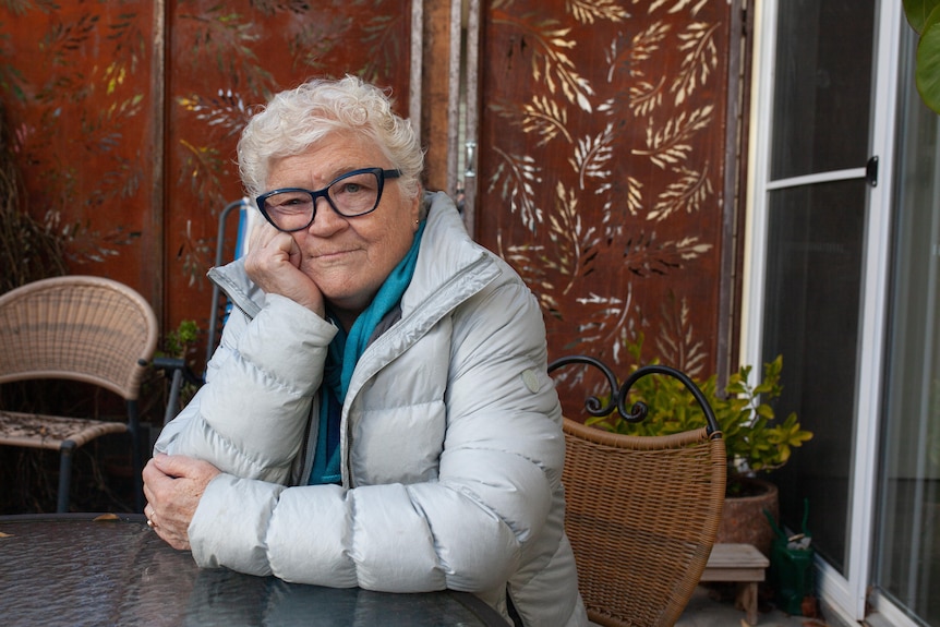 An elderly women leans on an outdoor table.