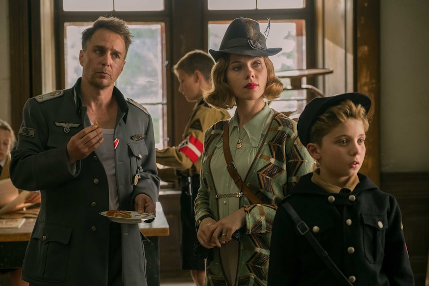 A man in Nazi uniform, a woman in a feathered hat, and a young boy in a button-up coat