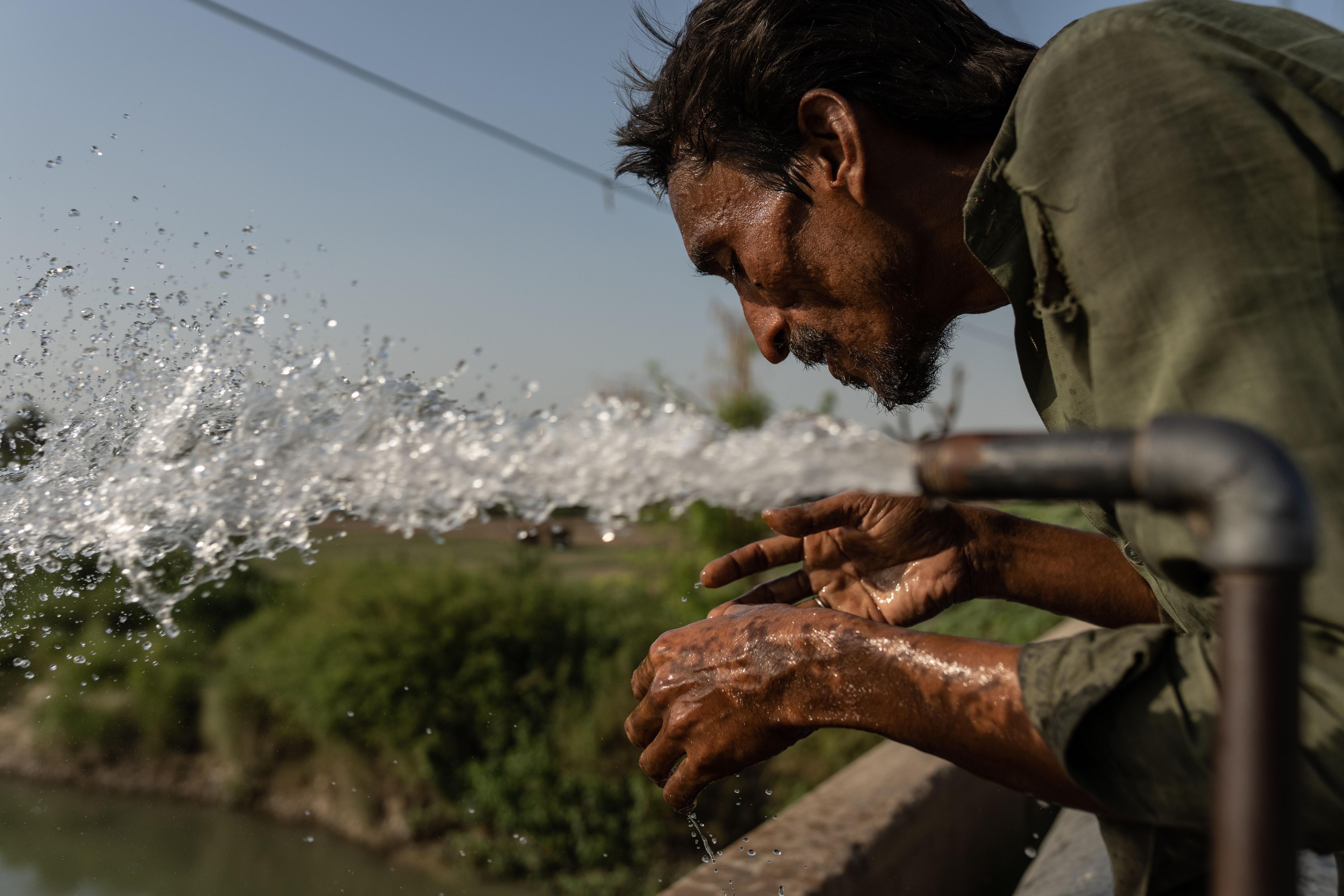Man with dark skin and hair leans over water pipe as a stream of clear water flows out over his hands.
