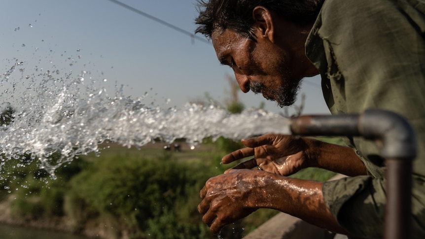 Man with dark skin and hair leans over water pipe as a stream of clear water flows out over his hands.