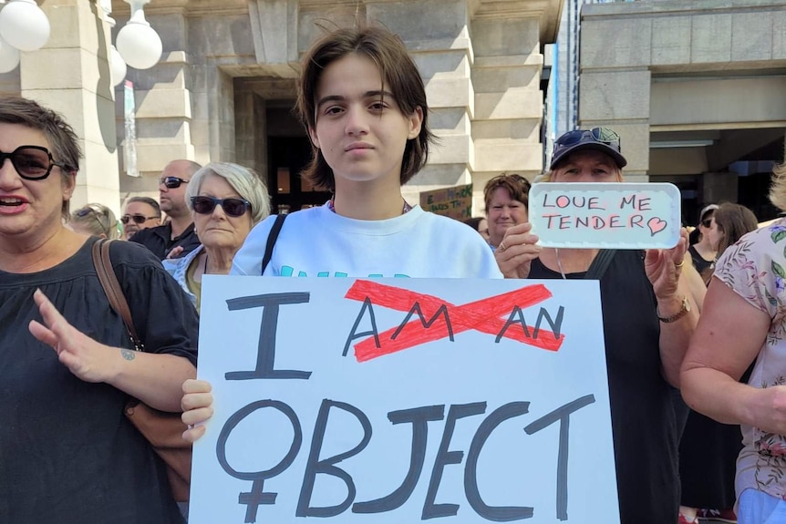 A sign at international women's day march reads "I object", with "am a" crossed out.