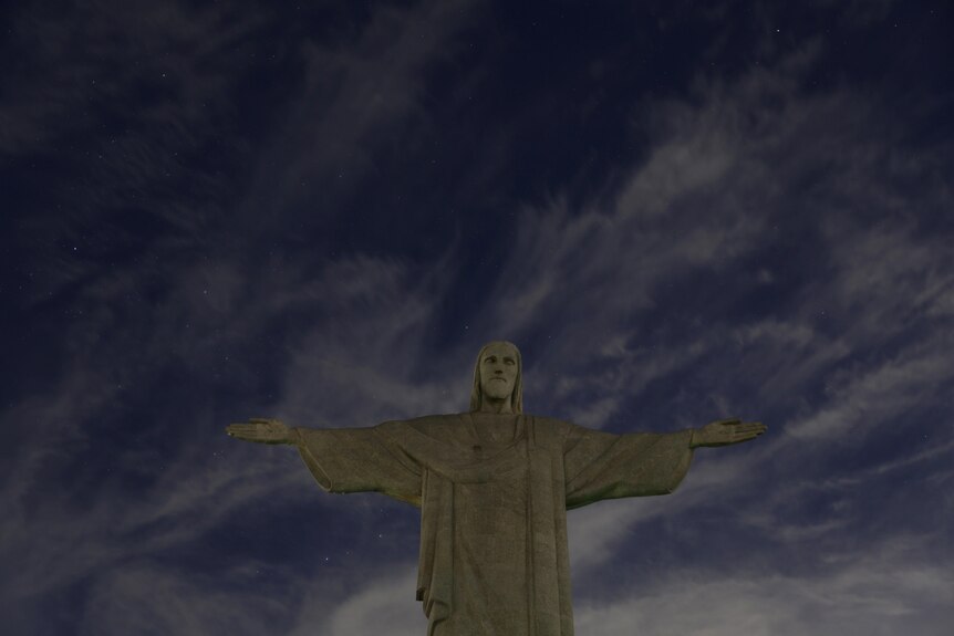 Stone statue of Christ the Redemeer without lights against cloudy dark sky. 