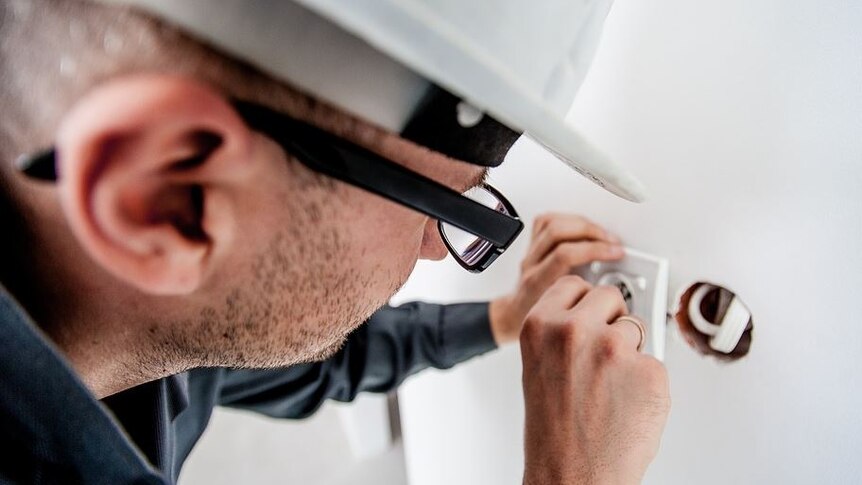 Picture of an electrician fixing a fitting in a white wall.  