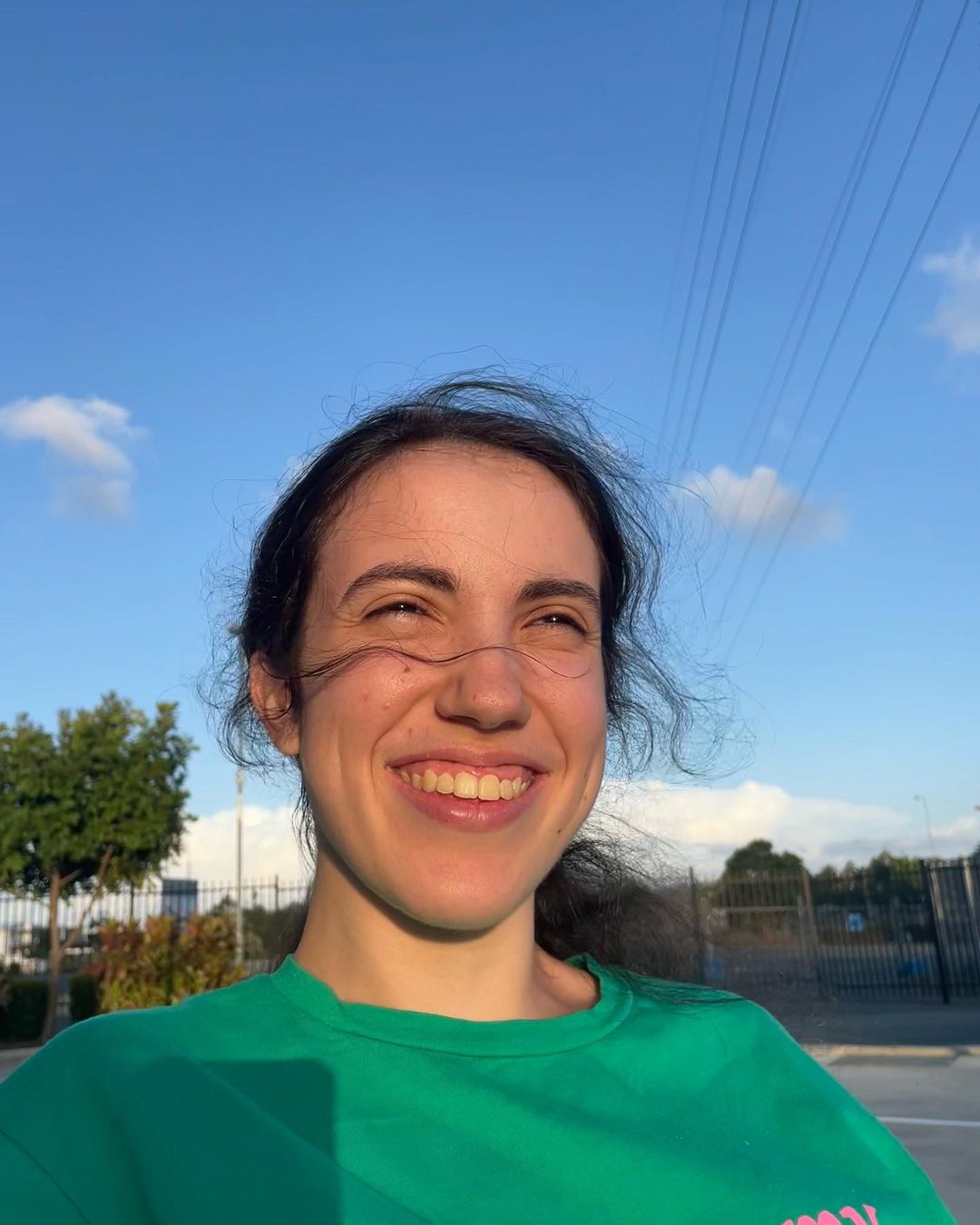 Writer Hannah Diviney outside, smiling as she looks into the distance, her hair blowing in the wind. Wearing a green t shirt.