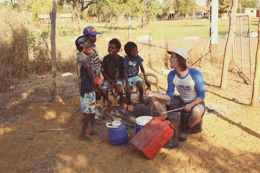 A group of kids watch on as a man hits objects with drum sticks.