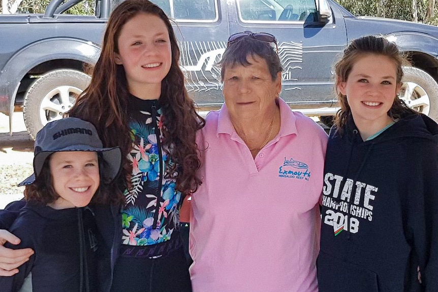 An older woman and three young children smiling at the camera standing at a caravan park