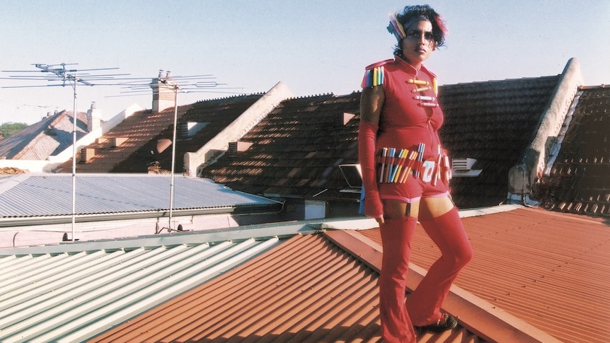 A woman with coloured felt-tipped pens attached to her clothing standing on the roof of a building.