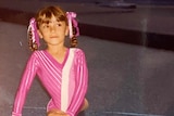 A young girl in a pink leotard doing the splits.