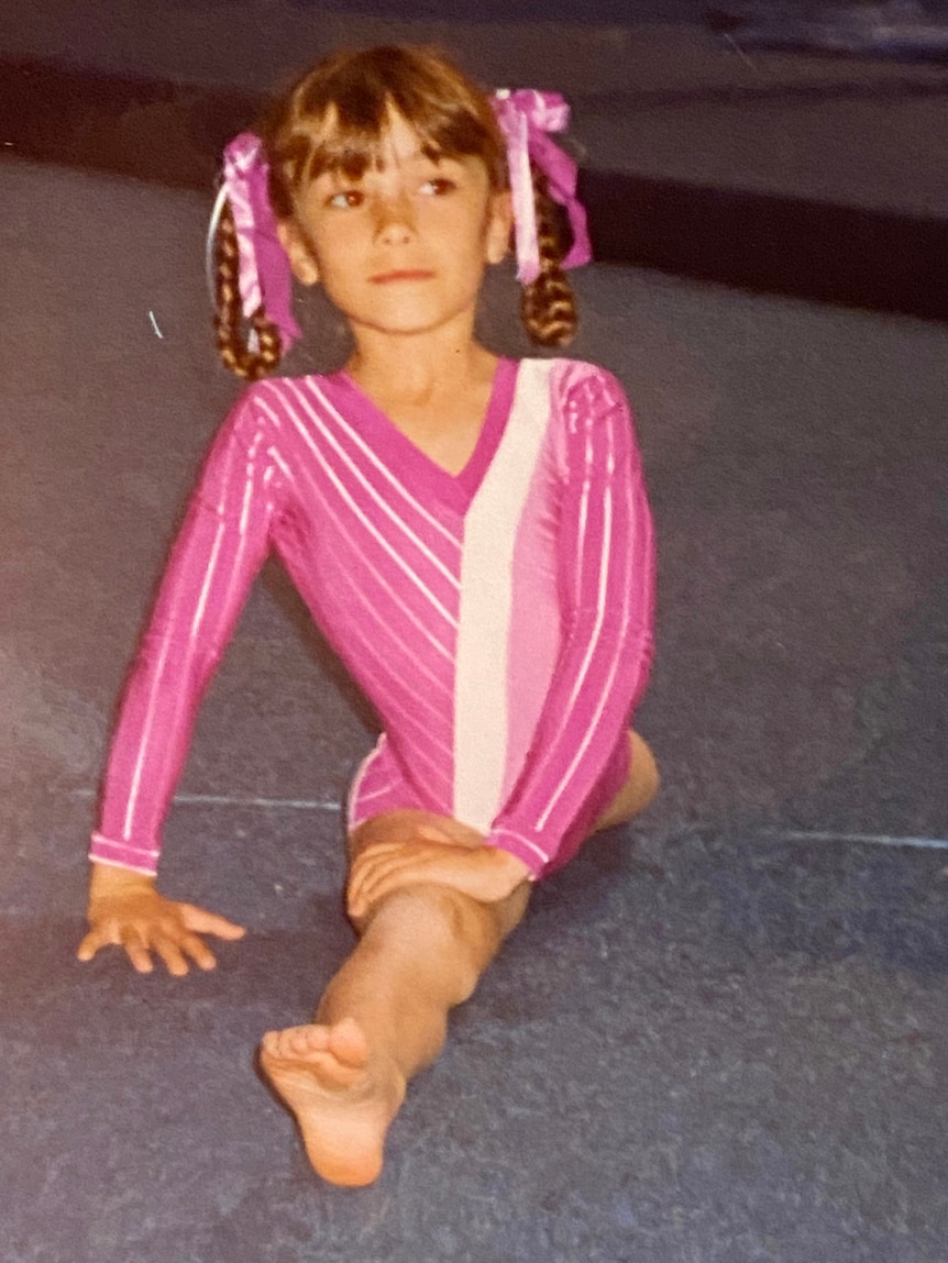 A young girl in a pink leotard doing the splits.
