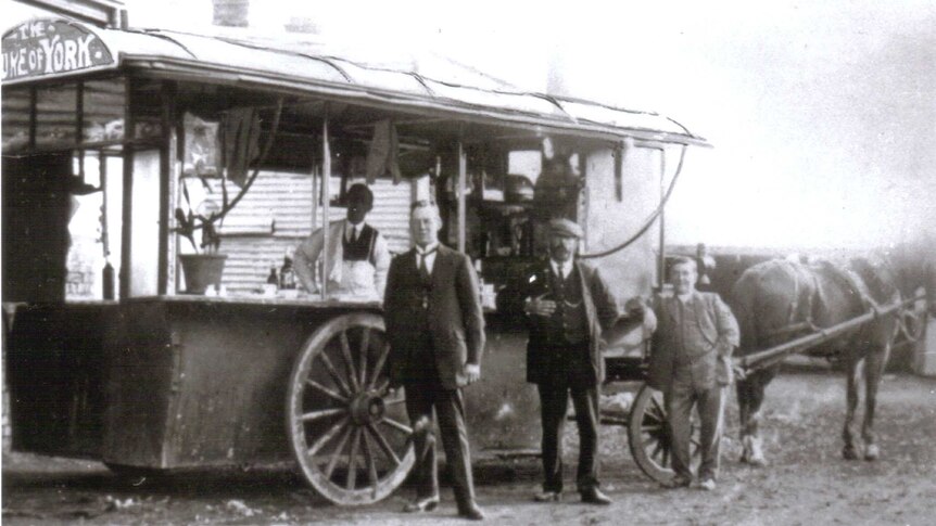 An historic photo of a man standing outside of a pie-cart being pulled by a horse