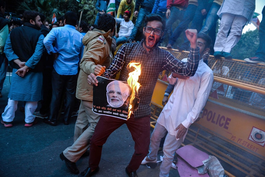 A young man holds picture of Narendra Modi on fire.