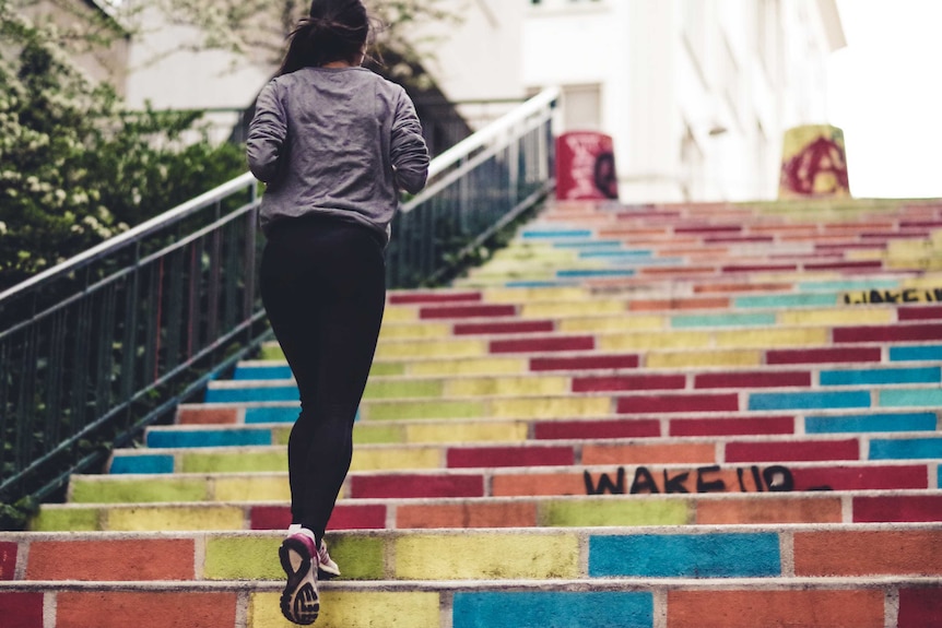 Woman in running clothes jogs up colourfully painted stairs.