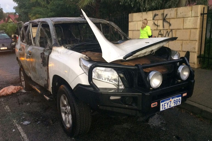 The burnt-out car in the foreground, with a woman removing offensive graffiti in the background.