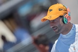 F1 driver Daniel Ricciardo wears a team cap and headphones as he looks down before a race.