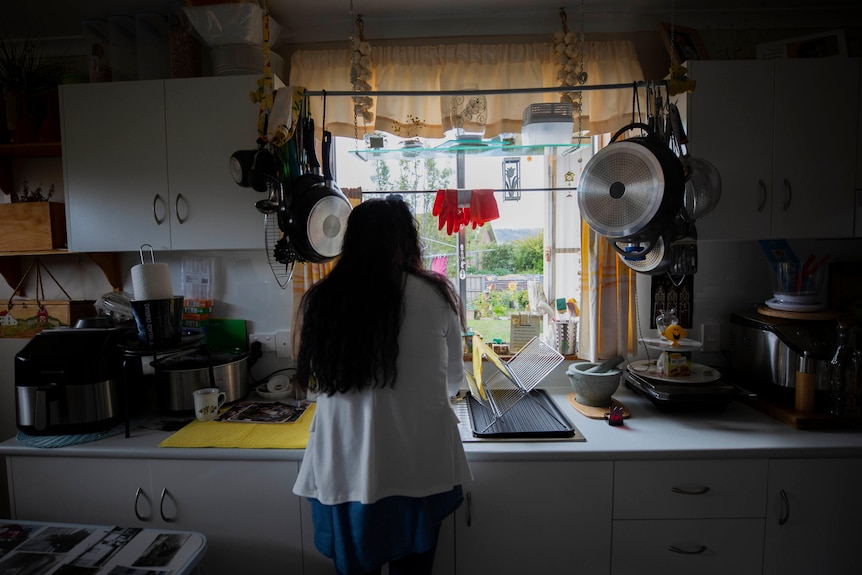 A woman stands back on at the sink in her kitchen