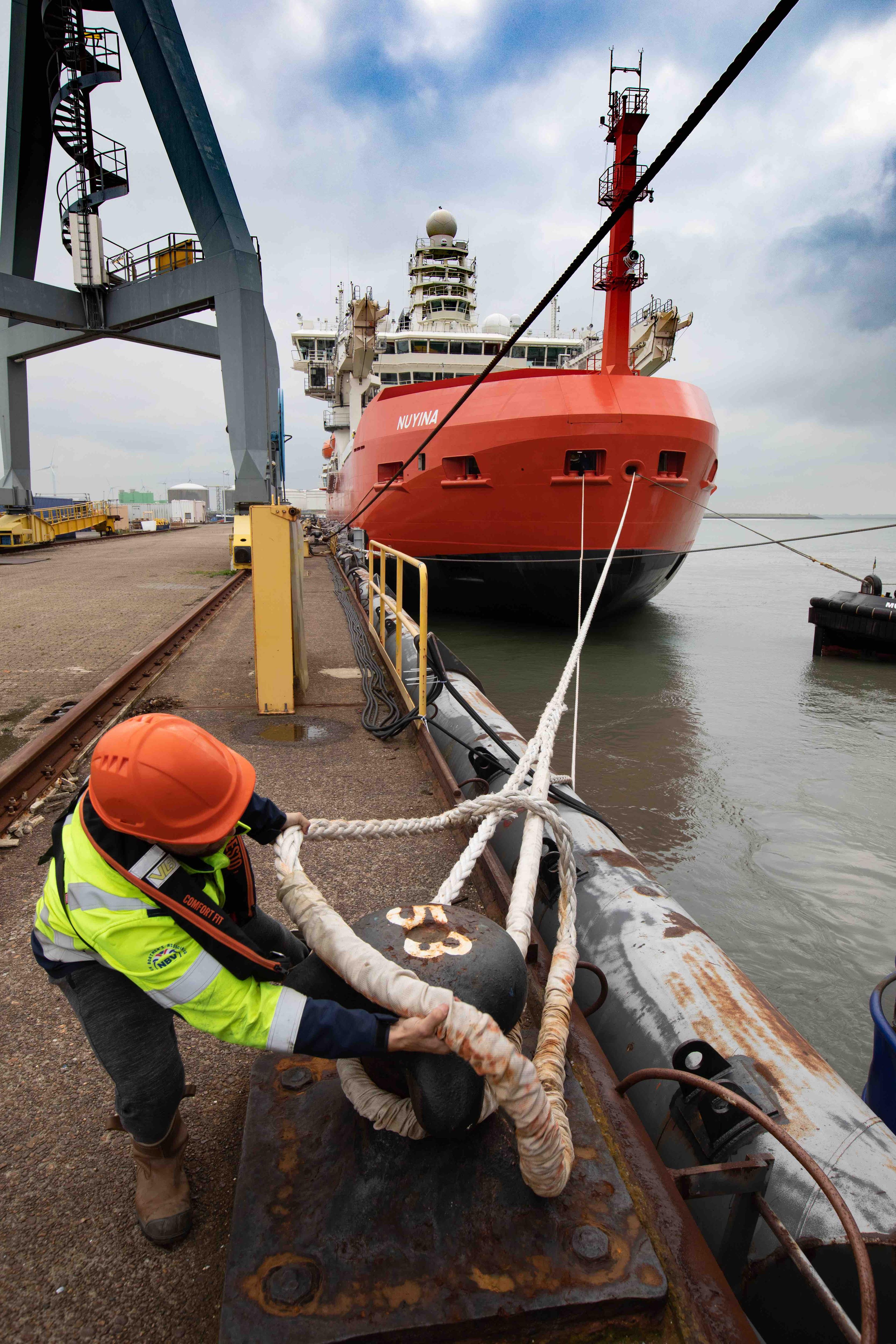 A worker removes a rope on a dock with an orange ship in the background.