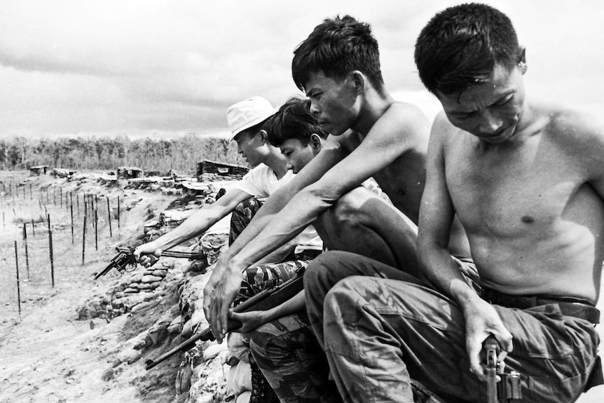 South Vietnamese soldiers holding guns, sitting on sand bags.