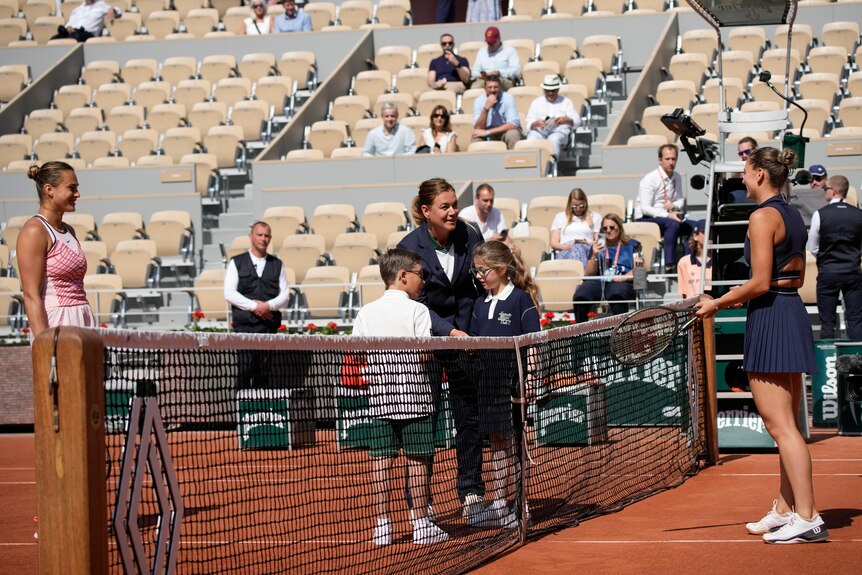 Two women stand on opposite ends of a tennis net, holding tennis racquets in their hands.