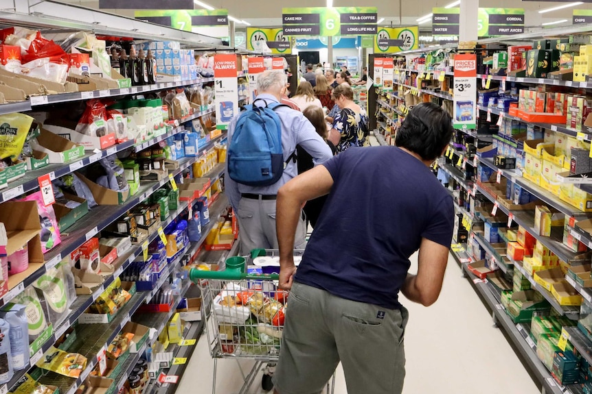 A line of shoppers with trolleys stretches down a supermarket aisle