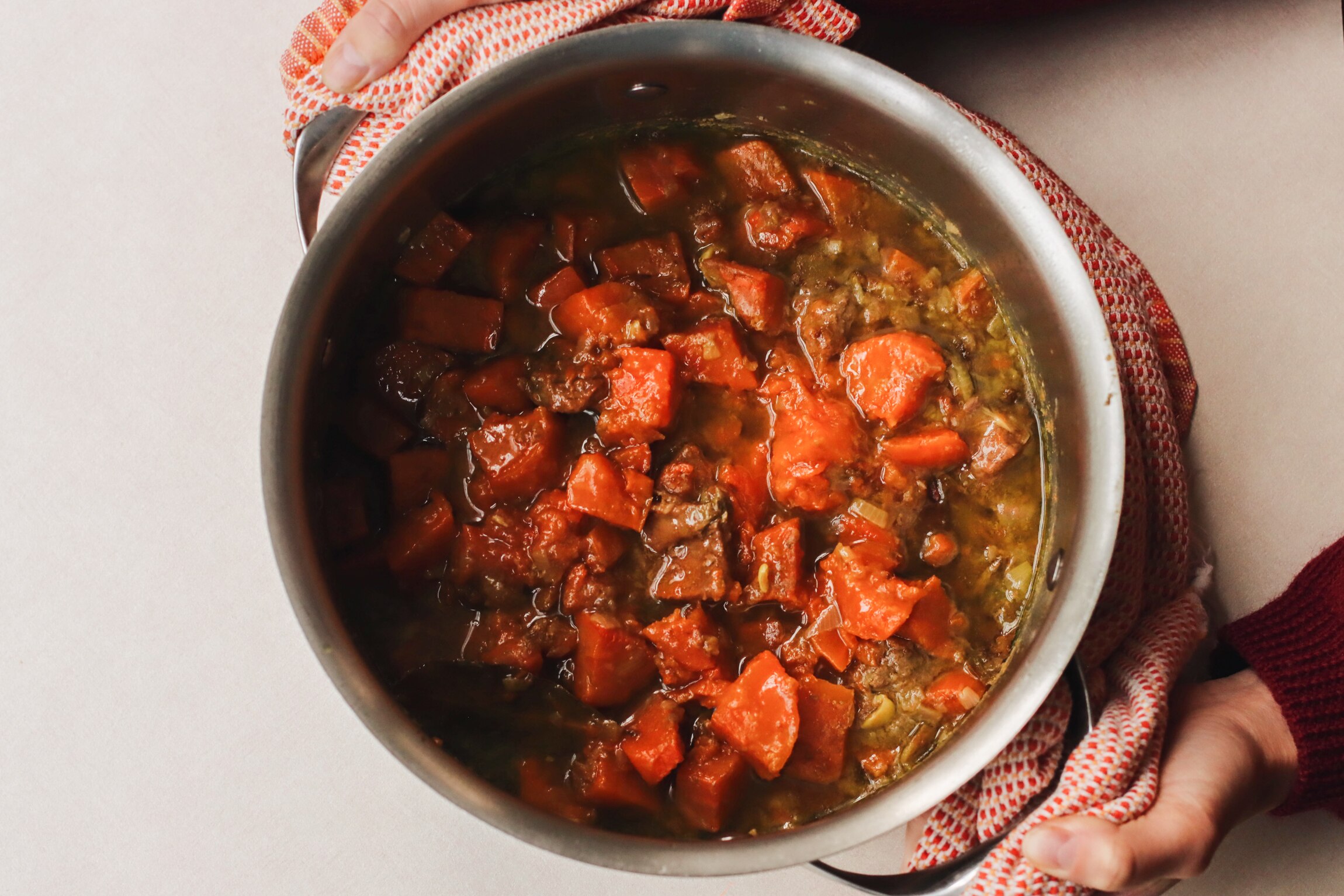 A pot of just-cooked beef and sweet potato stew, held by Heidi Sze using a tea towel. A filling family dinner.