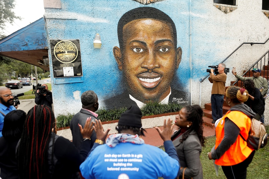 People gather at a wall with a mural painted of Ahmaud Arbery. 